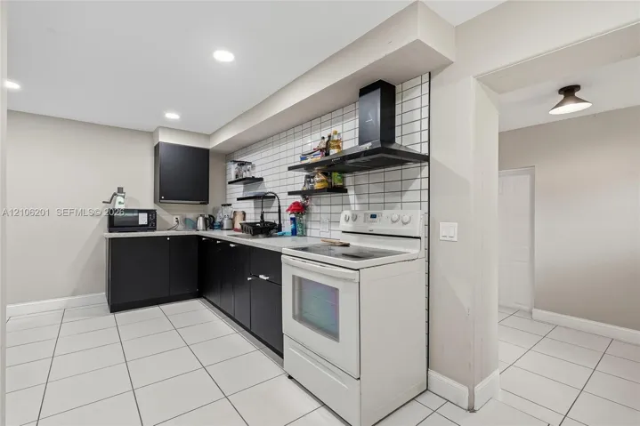 Kitchen featuring matte black cabinetry, white square tile backsplash, white ceramic tile flooring, built-in black range hood, and recessed lighting