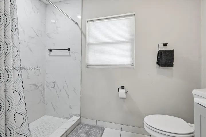 Full-height shower surround with stone-patterned tile, white hexagonal tile shower flooring, recessed window with blinds, and matte black hardware