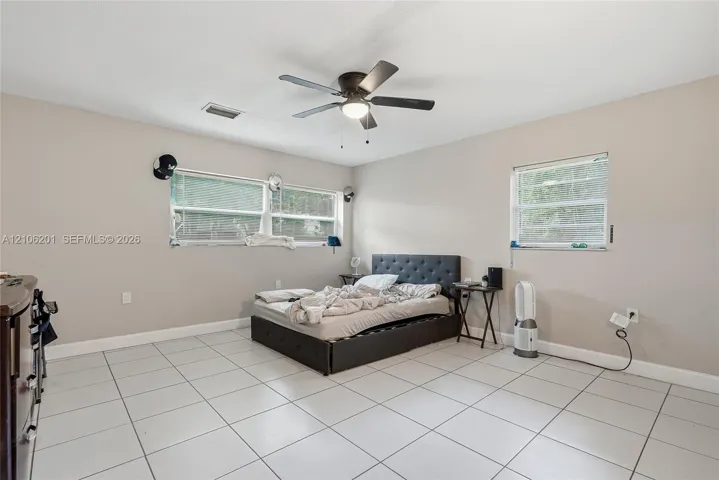 Neutral-toned interior featuring large-format ceramic floor tiles, three windows with horizontal blinds, and a central ceiling fan with an integrated light fixture