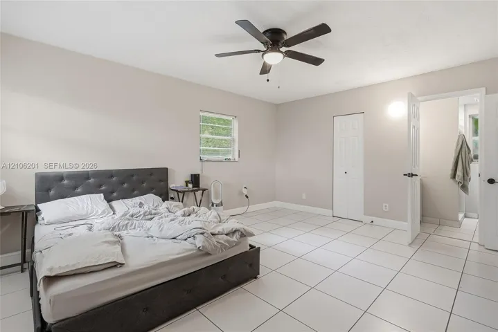 Neutral-toned room featuring large-format tile flooring, a centered ceiling fan with integrated lighting, and a dual-panel closet door