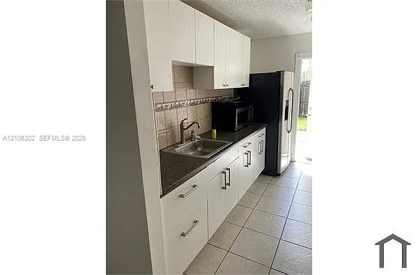 Kitchen featuring white cabinetry, dark countertops, tiled backsplash, stainless steel sink with a gooseneck faucet, and tile flooring