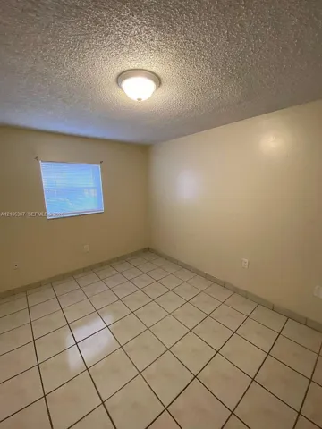 Neutral-toned room featuring ceramic tile flooring, textured ceiling finish, single-window configuration, and flush-mount lighting