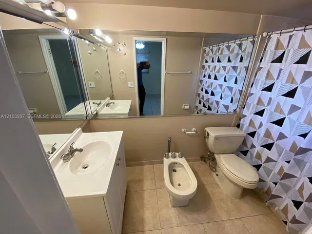 Bathroom featuring a white vanity cabinet with an integrated basin, large wall-mounted mirror, floor-mounted bidet, and neutral-tone tile flooring