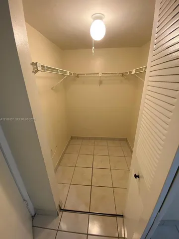 Storage area featuring tiled flooring, wall-mounted wire shelving, and a louvered door