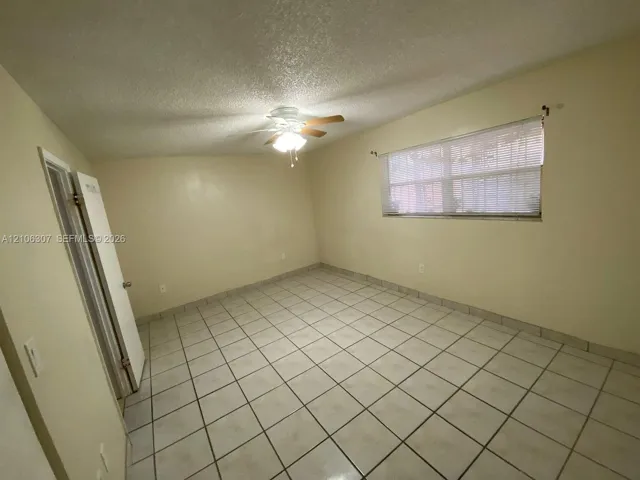 Neutral-toned room featuring large-format ceramic tile flooring, a centered ceiling fan with integrated light fixture, and a single window with horizontal blinds