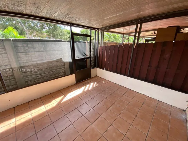 Enclosed patio featuring tile flooring, screened walls, and a wood privacy fence