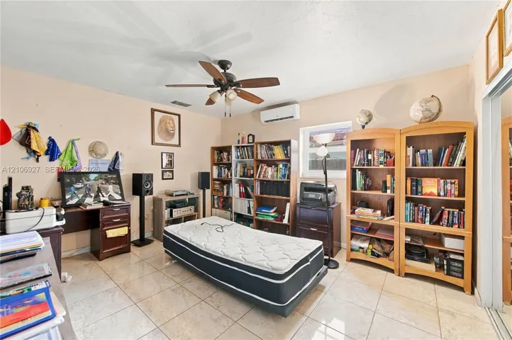Room featuring neutral wall paint, polished tile flooring, ceiling fan with integrated lighting, and a wall-mounted ductless air conditioning unit