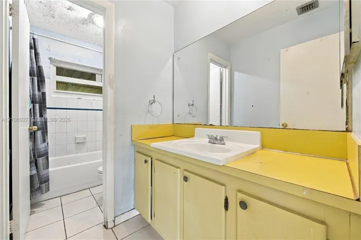 Bathroom featuring a vanity with a drop-in sink, a large wall-mounted mirror, ceramic tile flooring, and a tub-shower combination with tile surround