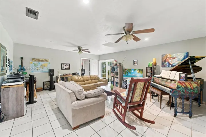 Spacious room featuring neutral-toned tile flooring, dual ceiling fans, and multi-pane glass french doors