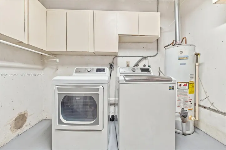 Utility space featuring white overhead cabinetry, dedicated washer and dryer connections, and a water heater