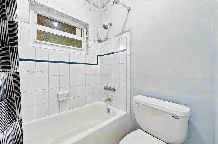Bathroom featuring a porcelain tub, wall-mounted shower head, white tiled surround with decorative trim, and a horizontal window
