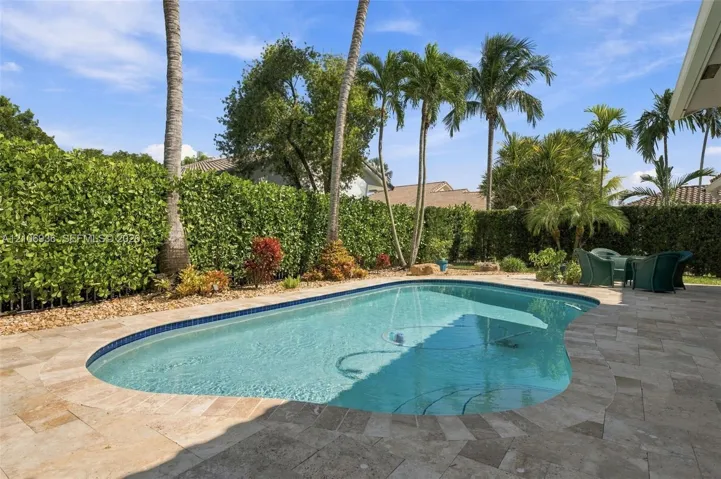 In-ground swimming pool with tile border, stone-finish patio decking, and perimeter privacy landscaping