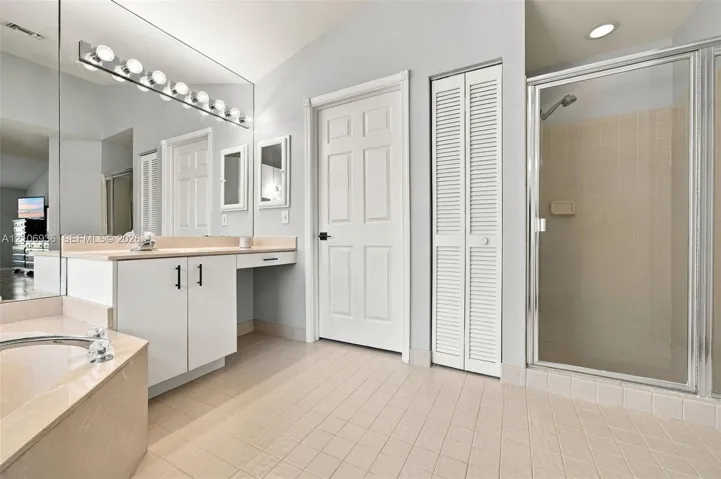 Bathroom featuring a tiled floor, walk-in shower with a glass enclosure, built-in vanity with a sit-down counter, and an expansive wall-mounted mirror with integrated light fixtures