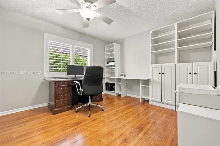 Custom built-in white cabinetry with open shelving and workspace, wood-finish flooring, and white plantation shutters