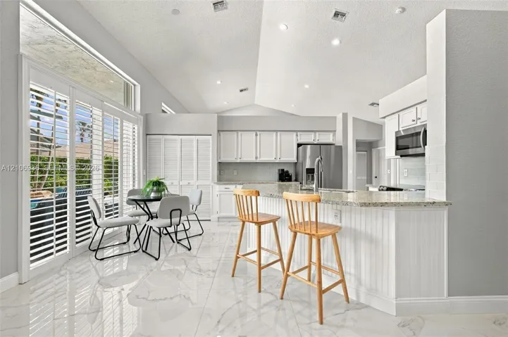 Kitchen featuring vaulted ceilings, stone-surface countertops, beadboard cabinet detailing, large-format tile flooring, and floor-to-ceiling sliding glass doors with plantation shutters