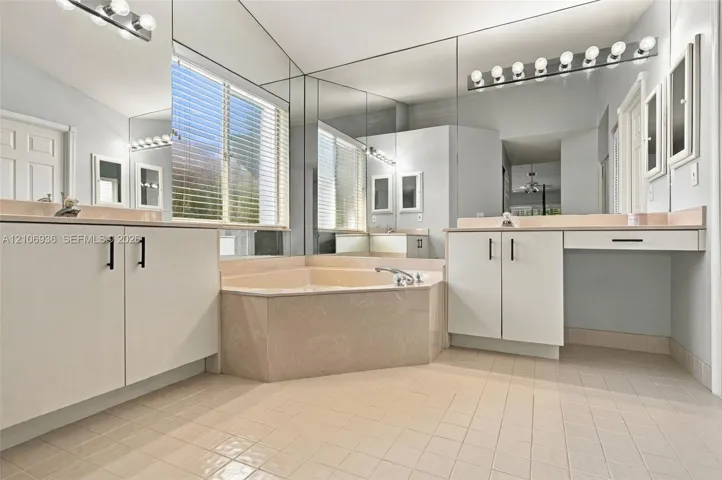 Bathroom featuring dual-sink cabinetry with matte black hardware, a tiled corner soaking tub, full-width wall mirrors, and integrated vanity lighting