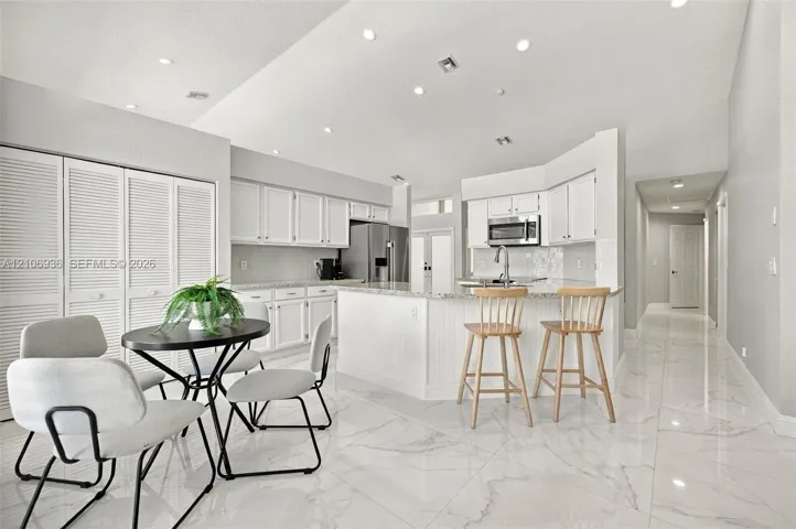 Kitchen featuring white cabinetry, stone-finish countertops, stainless steel appliances, a center island with bar seating, and large-format porcelain tile flooring