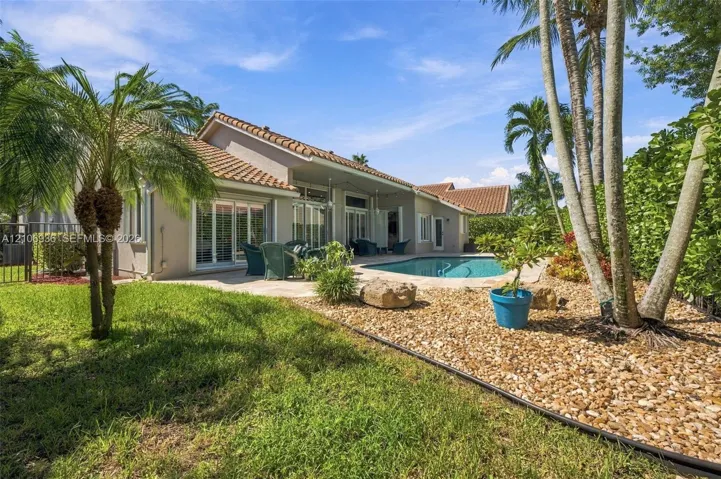 Rear exterior featuring a tile roof, an in-ground swimming pool, a concrete patio, and a landscaped yard with rock ground cover and palm trees