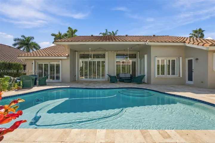 Swimming pool with integrated steps, expansive stone-paver patio, covered outdoor area, and multi-panel sliding glass doors