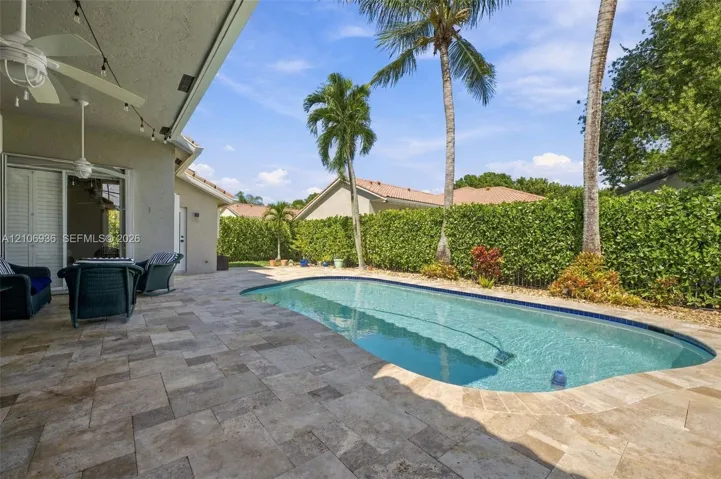 Covered patio with stone-paver flooring, built-in ceiling fan, swimming pool, and privacy-hedged perimeter
