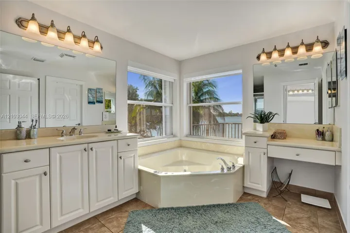 Bathroom featuring a corner soaking tub, dual vanity with stone countertops, integrated makeup vanity, and two large wall-mounted mirrors