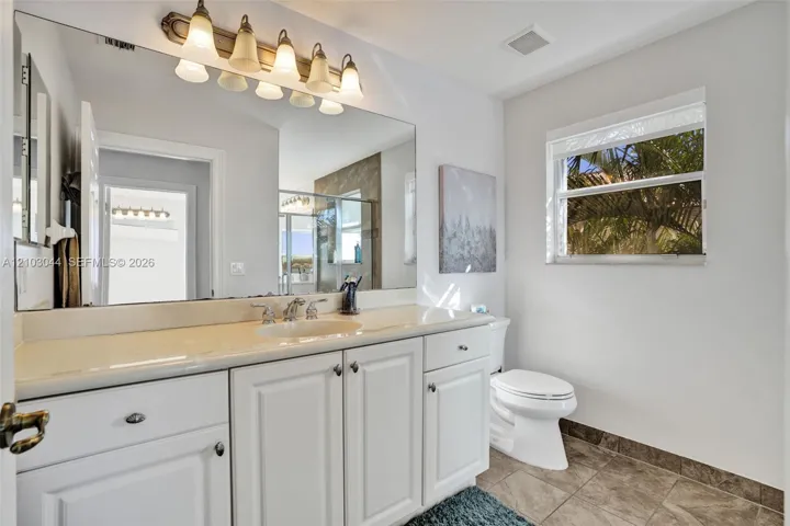 Bathroom featuring a white vanity with integrated basin, expansive wall-mounted mirror, five-light overhead fixture, and tile flooring