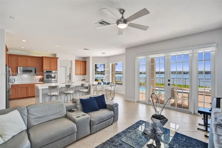 Open-concept living space featuring wood-finish cabinetry, a waterfall-edge center island with a built-in sink, recessed lighting, a modern ceiling fan, and sliding glass doors with exterior patio access
