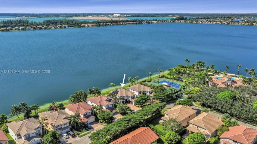 Aerial perspective of waterfront property featuring extensive shoreline access, tile roof construction, and proximity to community-maintained tennis courts