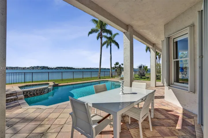Covered patio with stone-tile flooring featuring a built-in swimming pool, integrated spa, and metal perimeter fencing