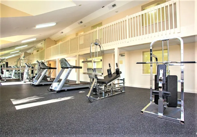 Fitness area featuring high ceilings, rubberized flooring, large mirrored wall panels, and an open loft gallery with white spindle railings
