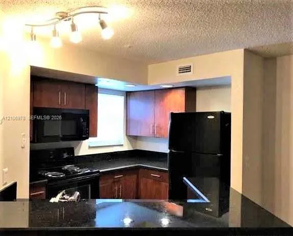 Kitchen featuring dark-finish cabinetry, solid surface countertops, black appliances, and multi-bulb overhead track lighting
