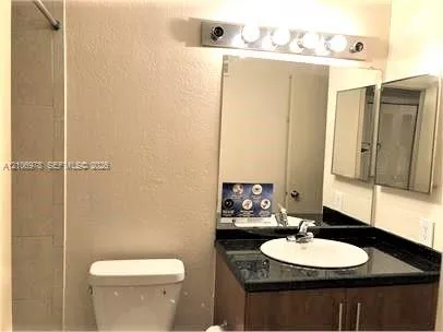 Bathroom featuring a wood-finish vanity with a stone-surface countertop, an integrated round sink, a large wall-mounted mirror, and a multi-bulb vanity light fixture