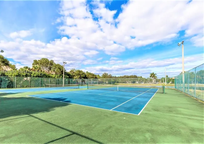 Dual hard-court tennis facility featuring perimeter chain-link fencing and overhead court lighting