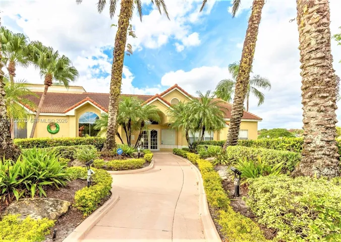 Stucco exterior featuring a tile roof, arched window, paved walkway, and mature palm trees