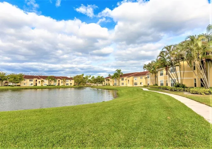 Multi-unit buildings featuring stucco exteriors, concrete tile roofing, manicured green space, a lake, and a paved walkway