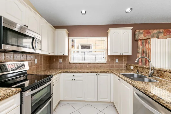 Kitchen featuring white cabinetry, stone countertops, square tile backsplash, recessed lighting, and stainless steel appliances
