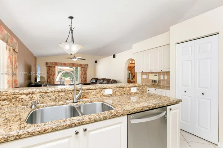 Kitchen featuring stone countertops, white cabinetry, stainless steel dishwasher, dual-basin stainless steel sink, and decorative pendant lighting