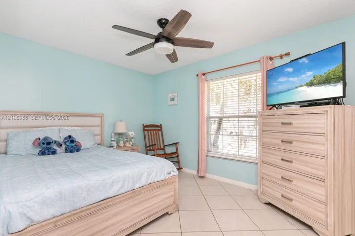 Neutral-toned tile flooring, horizontal window blinds, and a multi-blade ceiling fan with integrated lighting