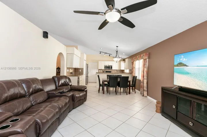 Open-concept interior featuring light-toned tile flooring, vaulted ceilings with a center-mounted ceiling fan, and track lighting