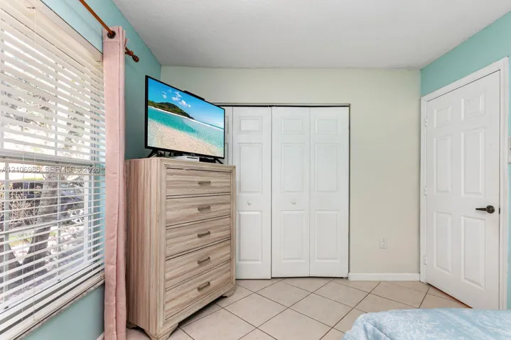 Ceramic tile flooring arranged in a diagonal pattern, white paneled bi-fold closet doors, a classic six-panel interior door, and a window with horizontal blinds