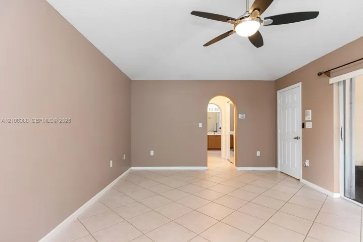 Room featuring ceramic tile flooring, a multi-blade ceiling fan with integrated lighting, a structural arched doorway, and a sliding glass door