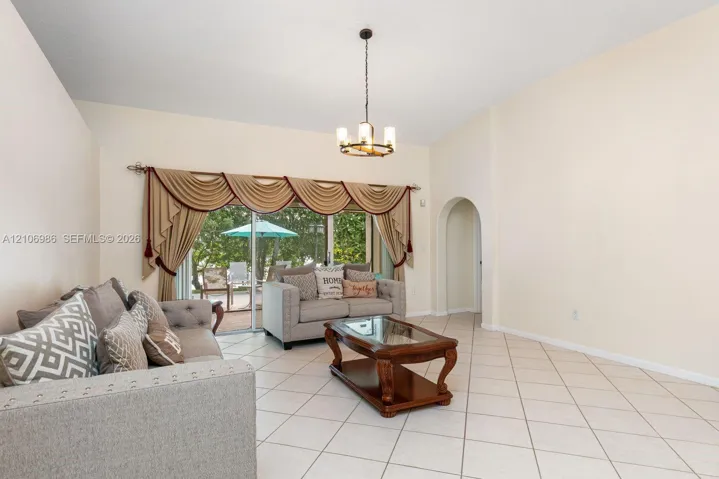 High-ceiling interior featuring light-colored ceramic tile flooring, a multi-arm candelabra-style chandelier, a recessed arched doorway, and a sliding glass door