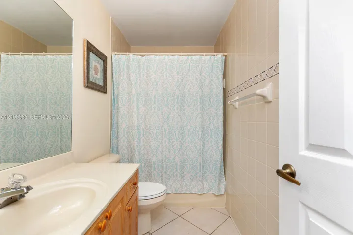 Bathroom featuring a wooden vanity with a stone countertop, an integrated sink, a large wall-mounted mirror, and tile flooring with decorative wall tile accents