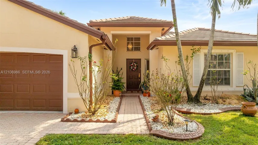 Stucco exterior with a tiled roof, paver driveway, walkway, recessed entryway, and attached garage