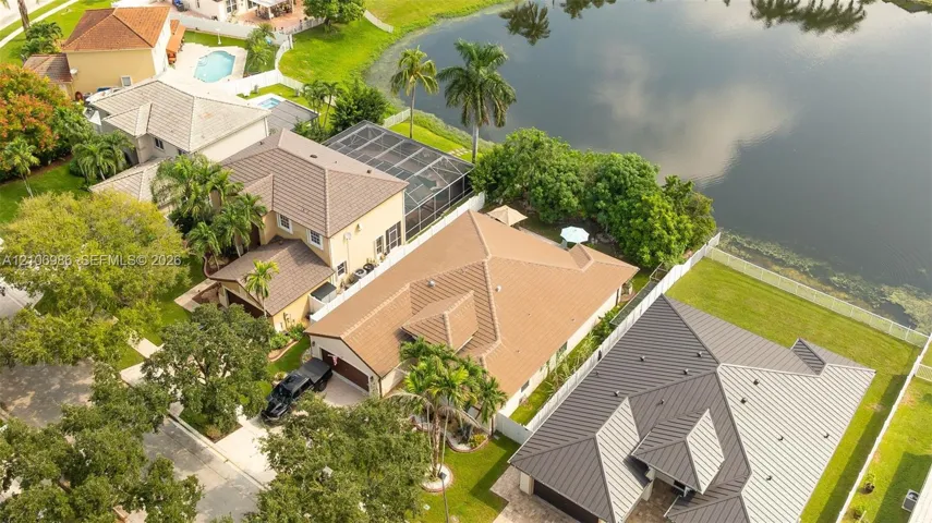 Aerial perspective featuring a tile roof, concrete driveway, attached multi-car garage, mature landscaping, and water frontage