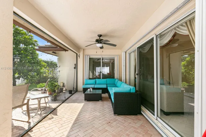 Covered outdoor patio featuring herringbone-patterned brick pavers, large multi-panel sliding glass doors, and a ceiling-mounted fan