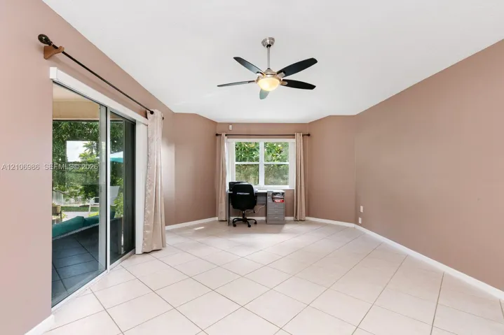 Room featuring light-toned tile flooring, large sliding glass doors, a dual-pane window, and a ceiling fan with integrated light fixture