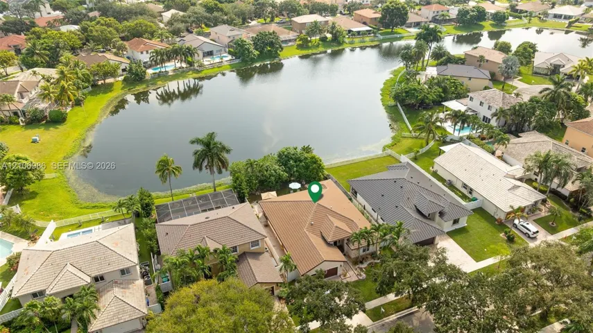 Aerial perspective of a multi-hip roofline property featuring a screened-in lanai, concrete tile roofing, and direct water frontage on a residential lake