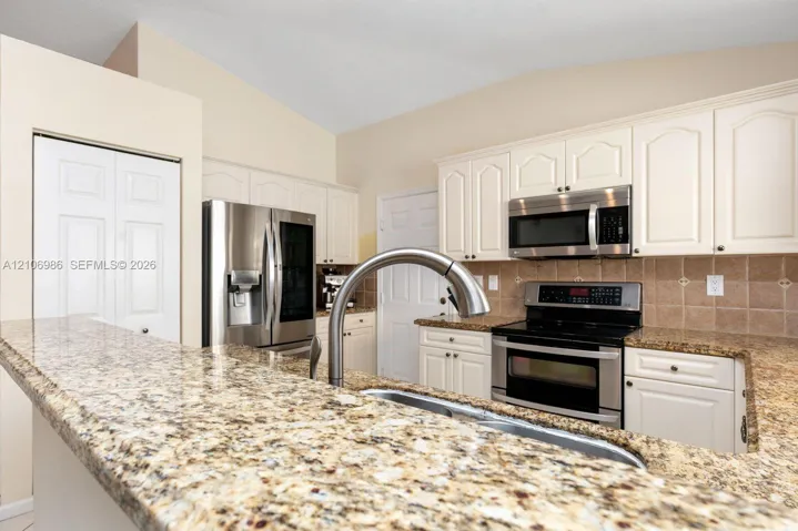 Kitchen featuring white cabinetry, stone countertops, a stainless steel refrigerator, a built-in microwave, and a high-arch gooseneck faucet