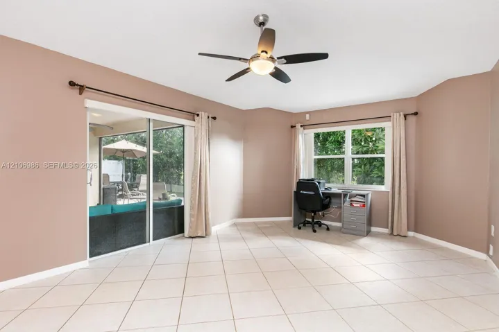 Large room featuring neutral tile flooring, a multi-blade ceiling fan with integrated lighting, sliding glass doors, and dual-pane windows